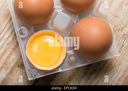 Gruppe von Eiern mit einem eröffnet mit Eigelb im Kunststoffkorb auf Holztisch Stockfoto
