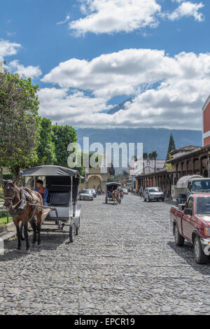 Straßenszene in Antigua Guatemala in der Nähe von Parque Central oder Central Park Plaza mit dem Vulkan Vulcan de Agua hinter teilweise in Wolken gehüllt. Stockfoto