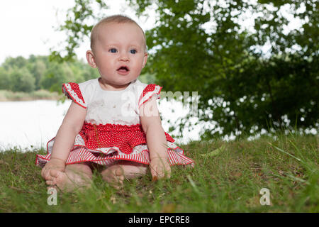 Kleines Mädchen sitzt und spielen am See Stockfoto