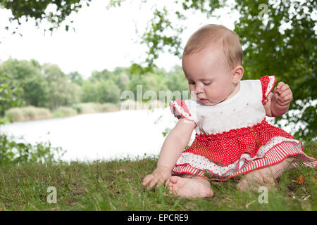 Kleines Mädchen sitzt und spielen am See Stockfoto