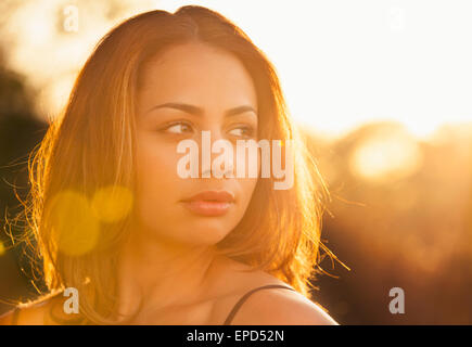 Rückseite beleuchteten Portrait mit Blendenfleck einer jungen Frau starrte in die Ferne an einem Sommertag bei Sonnenuntergang hinter ihr. Stockfoto