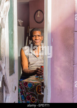 Ein Blick von außen in das Innere des Hauses von einem Afro-kubanischen Mann sitzt an einem Tisch mit s Erfrischungsgetränk nach vorne. Stockfoto