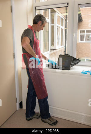 Männliche Besucher tragen schützende Kleid und Handschuhe auf NHS Station älteren Verwandten zu besuchen.  England, UK Stockfoto