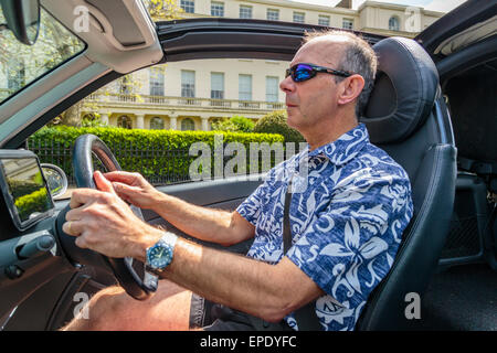 Ein Mann mittleren Alters, der an einem Sommertag im Regenten Park London England ein Cabriolet-Auto mit dem Dach nach unten fährt, trägt eine Sonnenbrille Stockfoto