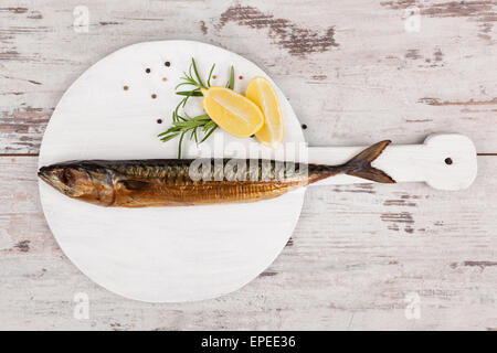 Leckere geräucherte Makrele Fisch an Bord Holzküche mit Zitrone, Rosmarin und bunten Pfefferkörner auf weiße strukturierte Holz Stockfoto