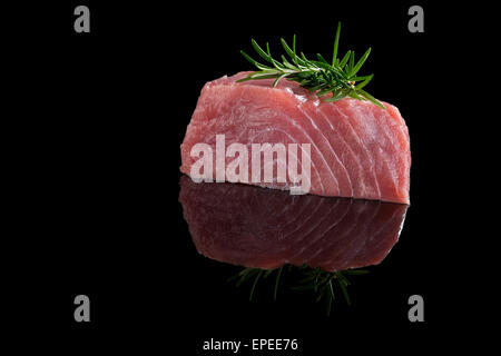 Thunfisch-Steak auf schwarzem Hintergrund isoliert. Rohen frischen Thunfisch-Steak mit Rosmarin Kräuter auf schwarz. Kulinarischen Thunfisch Steak Essen. Stockfoto