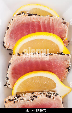Thunfisch-Scheiben mit Sesam und Zitronenscheiben auf weißen Teller. Kulinarischen Meeresfrüchte, gesund essen. Stockfoto