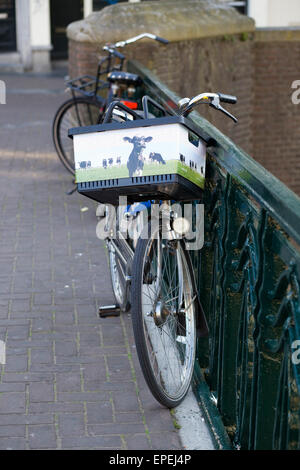 Fahrrad an einem Brückengeländer mit einem Korb mit einer Kuh auf der Vorderseite befestigt Stockfoto