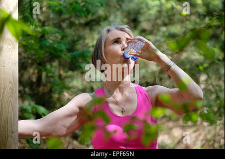 ältere Frau Trinkwasser aus der Flasche im Wald Stockfoto