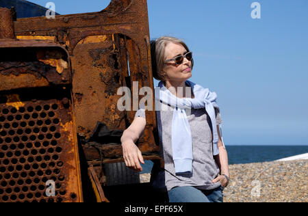 ältere Frau stützte sich auf rostigen Traktor am Strand Stockfoto