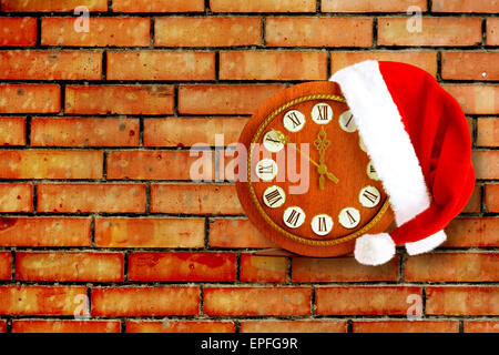 Weihnachtsmann Mütze am Silvester Abend auf der alten Uhr zeigt 12:00 auf dem Backstein-Hintergrund Stockfoto