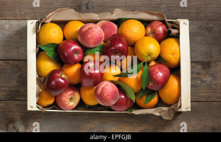 Orangen, Äpfel und Pfirsiche in einer Holzkiste auf eine Holzoberfläche. Stockfoto