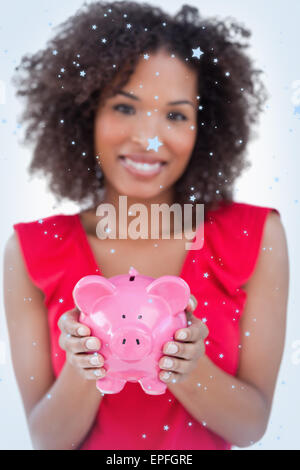 Zusammengesetztes Bild der Piggy Bank durch eine Brünette Frau statt Stockfoto