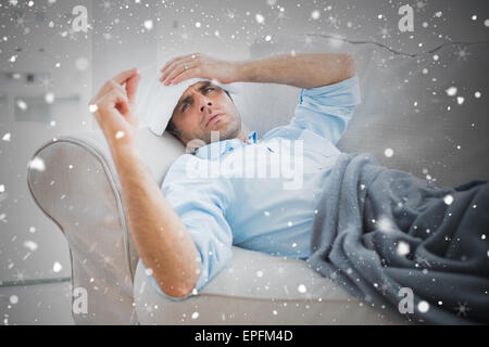 Zusammengesetztes Bild des kranken Mann auf Sofa überprüft seine Temperatur unter einer Decke Stockfoto