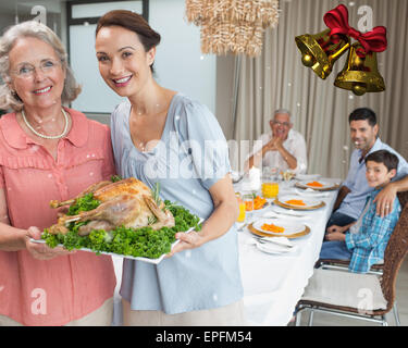 Frau und Großmutter hält Hähnchen braten mit Familie am Esstisch Stockfoto
