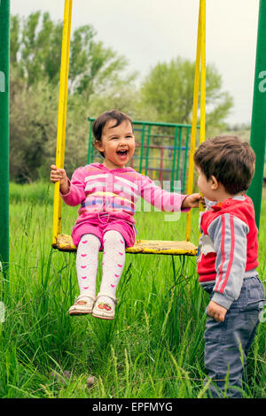 Zwei kleine Kinder, die Spaß auf einer Schaukel an Sommertag Stockfoto