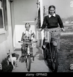 sitzen Sie 1950er-Jahren, historische, zwei Kinder, Bruder und Schwester, auf ihren Fahrrädern auf der Veranda außerhalb der eigenen Wohnung im mittleren Westen, der kleine Junge in einem Roy Rogers-Outfit gekleidet. Stockfoto