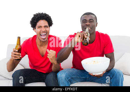 Fußball-Fans in rot jubeln auf der Couch mit Bier und popcorn Stockfoto