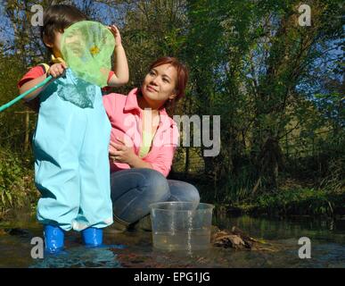 Kleiner Junge hielt seine Mutter Inspektion des Fangs in einem Fischernetz nach Eintauchen in einen Stream, Bristol, UK, November. Stockfoto