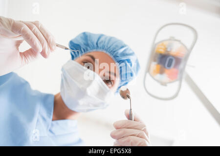 Zahnarzt in Mundschutz und Mütze hält Dentalwerkzeuge über Patienten Stockfoto