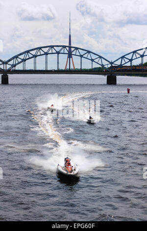 Motorboote mit Geschwindigkeit am Fluss Daugava in Riga auf dem Hintergrund des Zuges auf der Brücke und ein Fernsehturm Stockfoto