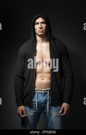 starker Mann mit schwarzer Hoodie isoliert auf dunklen Stockfoto