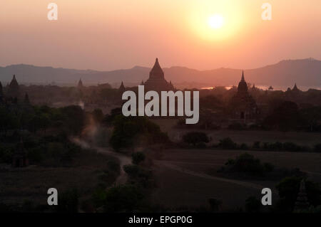 Die dunklen Silhouetten der steinernen Tempel gegen die gelben Schein der untergehenden Sonne in Bagan Myanmar Stockfoto