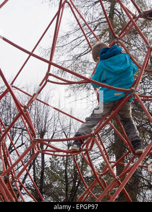 Young trittsicher junge klettern einen krakeligen Seil-Apparat auf einem norwegischen Spielplatz Stockfoto