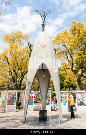 Touristen und Besucher der Kinderfriedensdenkmal-Statue mit dem Papierkran dahinter, im Friedenspark in Hiroshima. Stockfoto