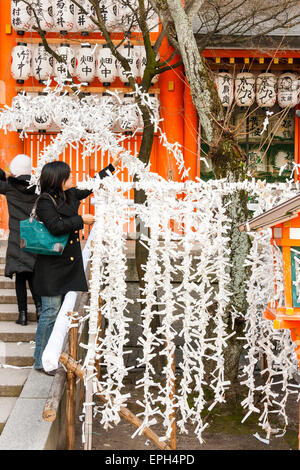 Leute, die Omikuji Papiertüchtschleine binden, stemmen während des Neujahrsfestes am Yasaka Shinto-Schrein in Kyoto quer über das Gerüst. Stockfoto