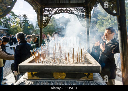 Chion-in Tempel in Kyoto. Mann, der am Räuchergefäß steht und den Rauch von schwelendem Räucherwerk, Osenko, winkt, klebt über sich. Stockfoto