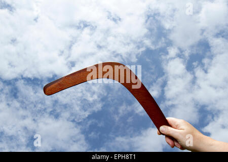 Hölzerne Bumerang in der Hand mit blauem Himmel und Wolken Hintergrund. Stockfoto