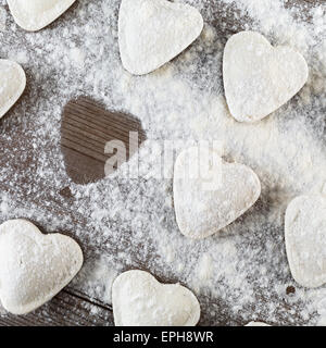 Ravioli kochen.  Rohe Klöße in Form von Herzen, bestreuen mit Mehl, auf dunklen Holztisch. Ansicht von oben. Stockfoto