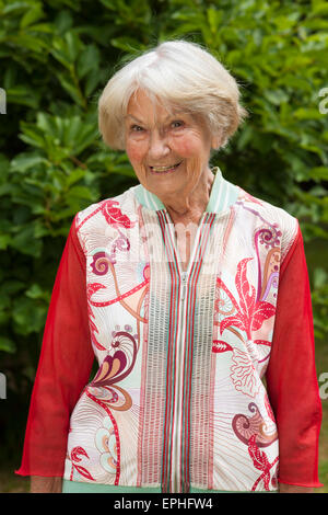 Stilvolle ältere Dame im trendigen rot oben stehen in ihrem üppigen grünen Garten in der Sonne in die Kamera Lächeln. Stockfoto