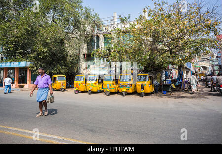 Lokalen indischer Mann beim Überqueren der Straße vor einer Reihe von geparkten gelbe Auto-Rikschas-Taxi cabs, Straßenszene, Chennai, Tamil Nadu, Indien Stockfoto