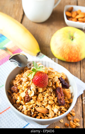 Gesundes Frühstück mit Vollkorn-Müsli, Früchten, Nüssen und Milch über rustikalen Holztisch Stockfoto