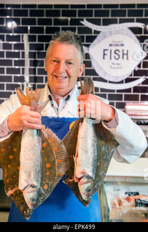 Ein Fischhändler an seiner Theke mit Scholle und Wolfsbarsch UK Stockfoto