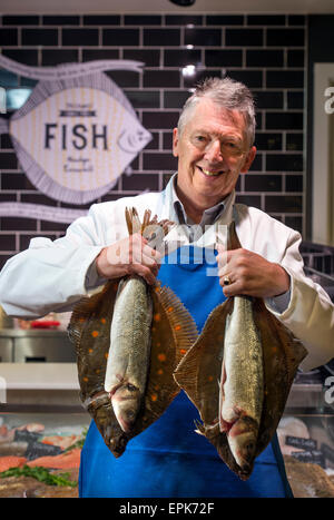 Ein Fischhändler an seiner Theke mit Scholle und Wolfsbarsch UK Stockfoto