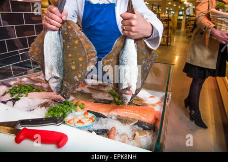 Ein Fischhändler an seiner Theke mit Scholle und Wolfsbarsch UK Stockfoto