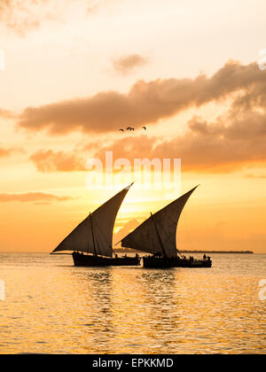 Zwei traditionelle tansanische Dhow Boote auf dem offenen Meer am Indischen Ozean in der Nähe von Stone Town auf Sansibar, bei orange Sonnenuntergang. Stockfoto