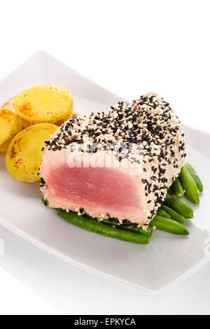 Gegrilltes Thunfischsteak eingehüllt in schwarzen und weißen Sesam auf grünen Bohnen mit Kartoffeln auf weißem Teller auf weißem Hintergrund. Stockfoto