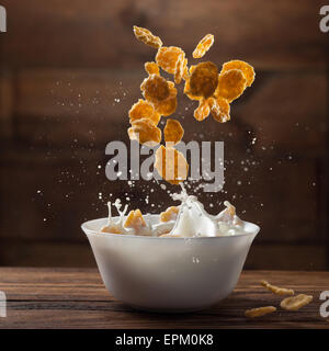 Fallende Cornflakes mit Milch Spritzen auf Holz Stockfoto