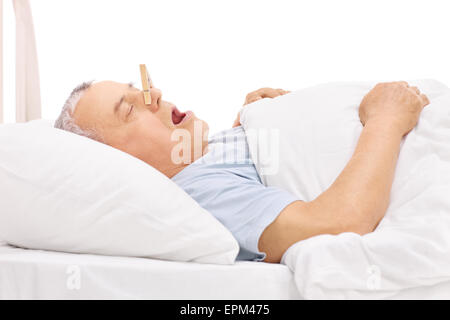 Senior in einem Bett schlafen und Schnarchen mit einer Wäscheklammer stecken auf der Nase isoliert auf weißem Hintergrund Stockfoto