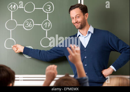 Lehrer an der Tafel mit Rechenaufgabe lächelnd Stockfoto