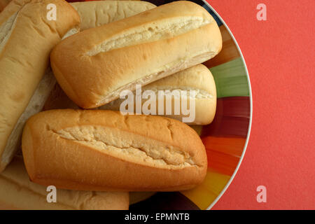 Blick auf mehrere frisch gebackene Bratwurst-Brötchen auf einem bunten Teller auf eine orange Tischplatte in der Nähe. Stockfoto