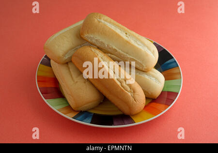 Frisch gebackene mehrere Bratwurst-Brötchen auf einem bunten Teller auf eine orange Tischplatte. Stockfoto