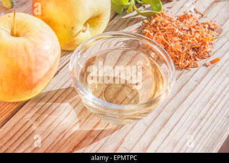 Eine Glasschüssel voll mit Apfelessig vor Äpfeln und Kräutern Stockfoto