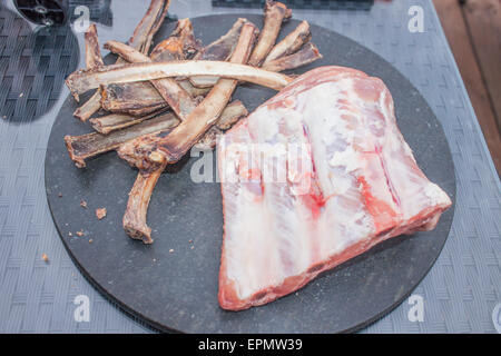 Schweinerippchen auf einer Steinplatte vor Rippenknochen Stockfoto