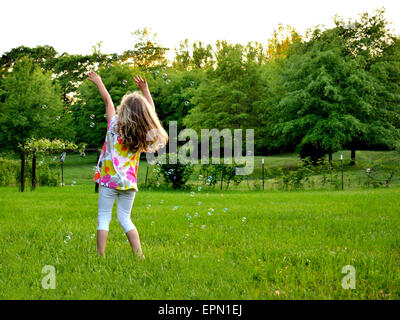 Junge Mädchen spielen mit Luftblasen, die in der Luft schweben Stockfoto