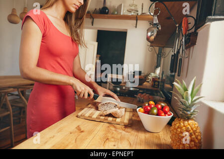 Aufnahme einer jungen Frau ein frisch gebackenes Brot auf einem heimischen Küchentisch schneiden beschnitten. Weibliche macht Frühstück Stockfoto